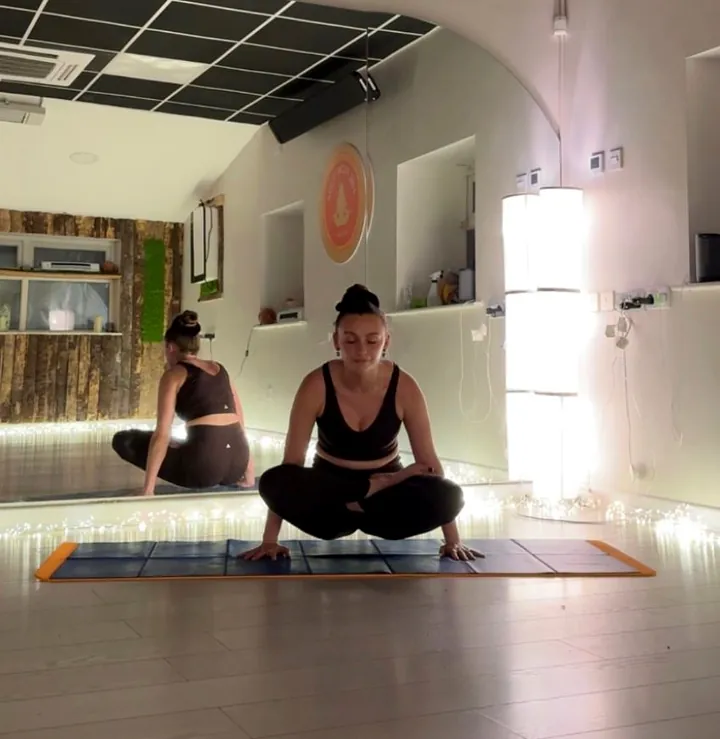 A student seated on a mat in front of the studio mirror, fairy lights along the floor