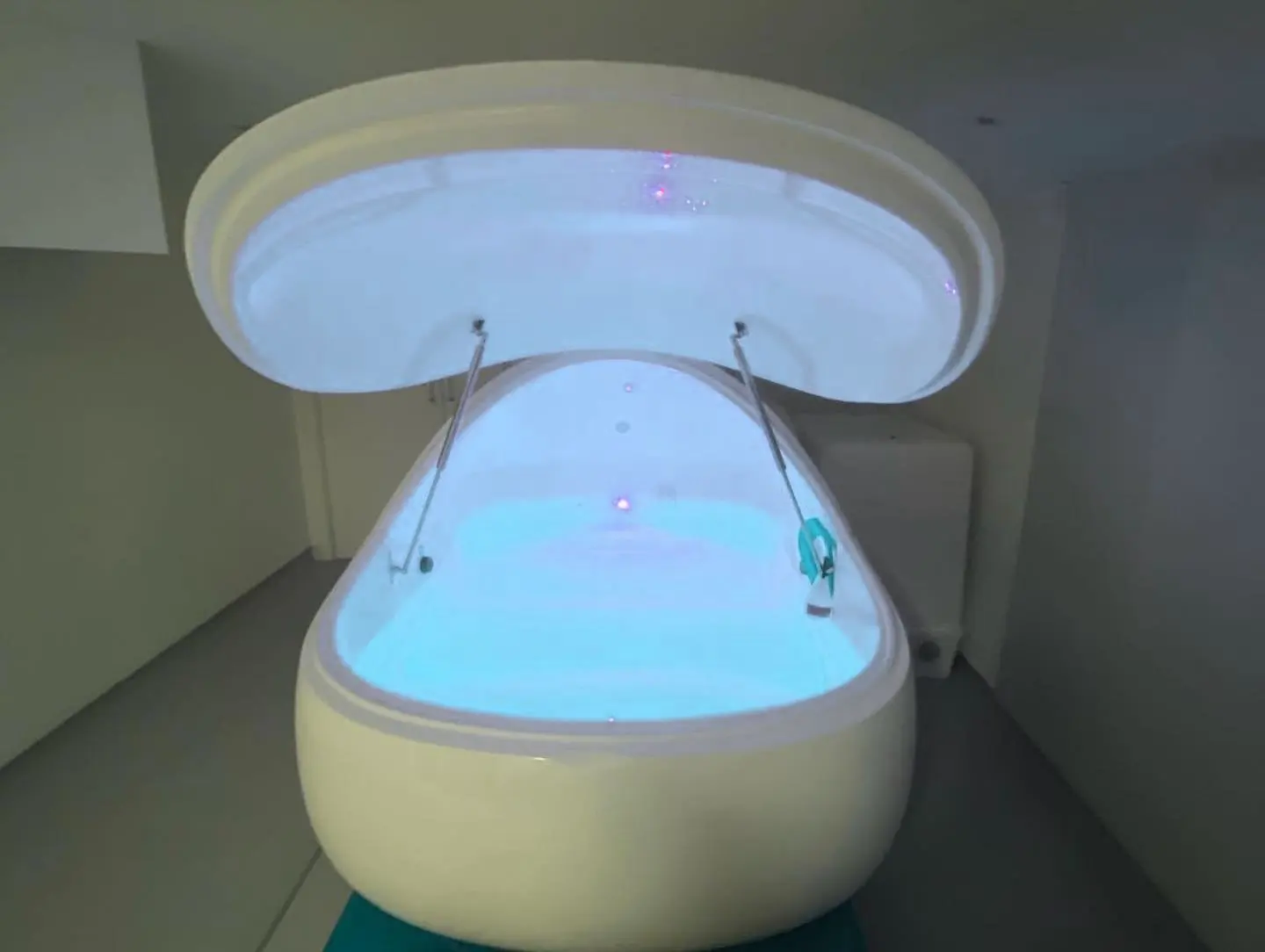 The pod seen from the front, lid up, in a quiet grey room.