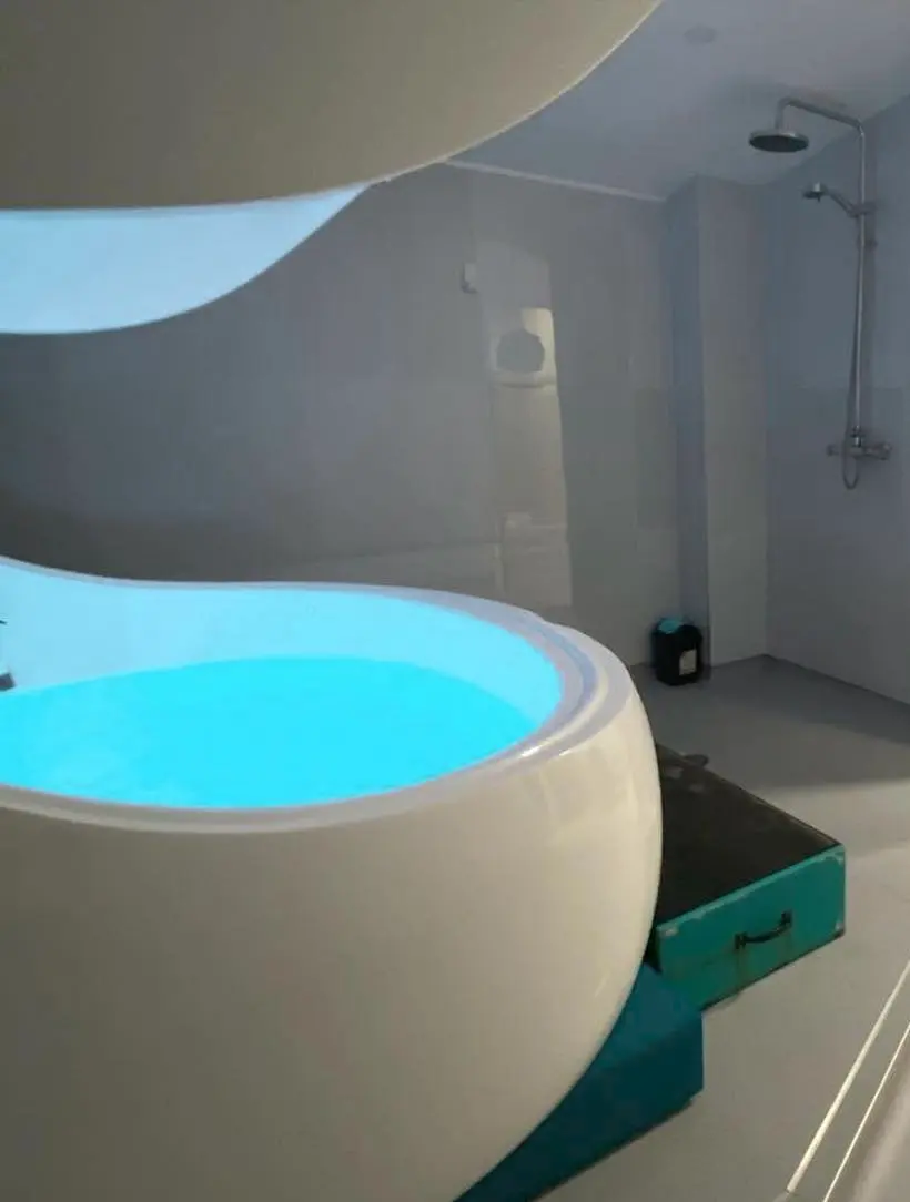 A float room: the white pod, a rain shower behind glass, a chair and towels.