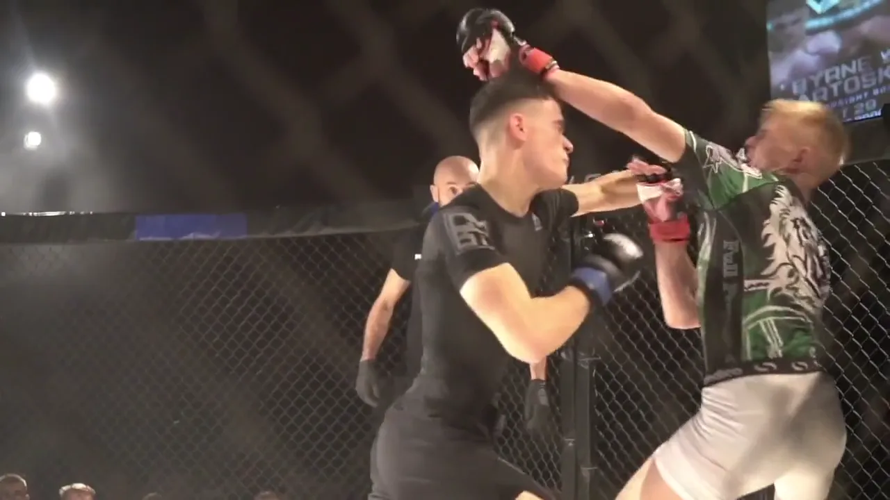 Two fighters trade strikes against the cage wall on a Holohan fight night: a right hand lands